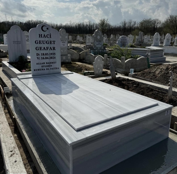 Мюсюлмански паметник с формата на джамия с полумесец и звезда, надпис с вдълбани черни букви, постамент, покривна плоча, висок облицован бордюр, бетонна основа