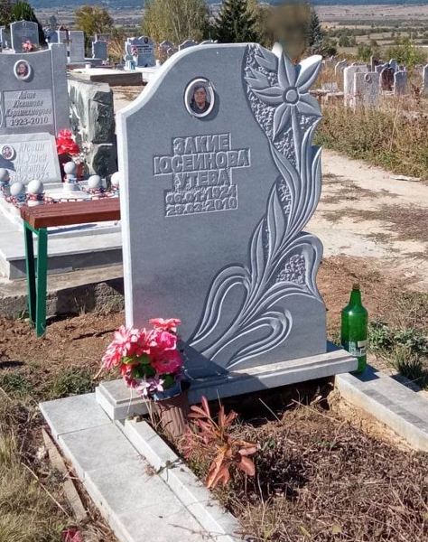 Паметник от сив мрамор, модел с голямо релефно цвете по диагонал на цялата височина, с порцеланова снимка и надпис, постамент и масивни бордюри, мраморна пътека.